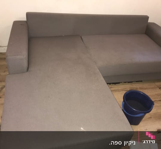 ספה אפורה עם דלי מים כחול על הרצפה
